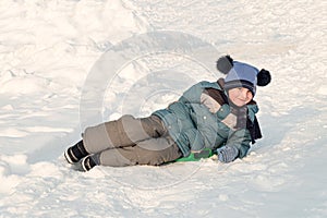 Child slid down a snow slide and is happy lies on an ice-boat