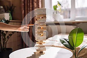 A child slides a wooden block of Jenga game on a white table under sunlight