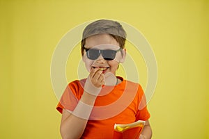 The child smiles and eats french fries on a yellow background. The boy holds in his hands his favorite food fries