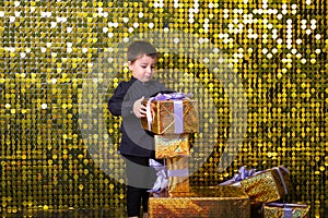 child smiling boy holding gift box on background with gold shiny sequins, paillettes