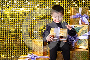 child smiling boy holding gift box on background with gold shiny sequins, paillettes