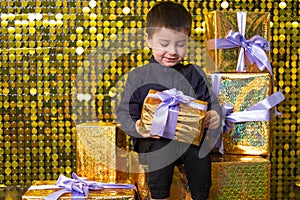 child smiling boy holding gift box on background with gold shiny sequins, paillettes