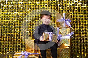 child smiling boy holding gift box on background with gold shiny sequins, paillettes