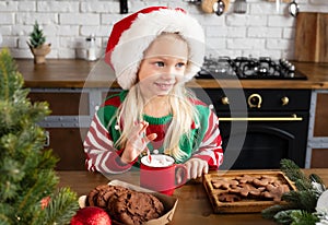 child smiling and looking sideways at wooden table with red mug of hot chocolate