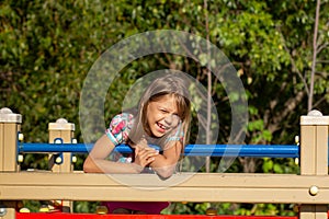 Child smiling and winking looking at camera on play ground over green trees