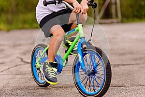 A child in sneakers pedaling a two-Wheeler on the asphalt in the summer. only feet on the pedals of the bike