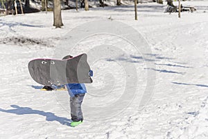 Child with a snowboard scrambles up a hill in a snow-covered par