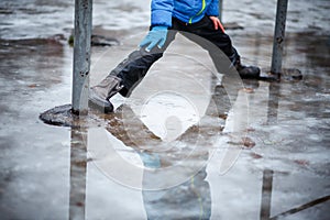 A child in snowboots boots is standing in a puddle of melted snow. Ice on the roads in the city. Not cleaned from snow and ice