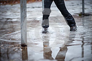 A child in snowboots boots is standing in a puddle of melted snow. Ice on the roads in the city. Not cleaned from snow and ice photo