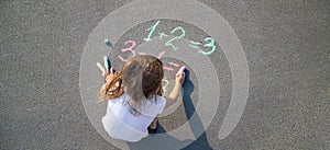 The child solves equations on the asphalt with chalk. Selective focus.