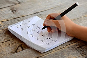 Child solves mathematics examples. Child holds a black marker in his hand. Notebook sheet with multiplication table examples