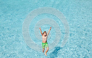 Child splashing in summer water pool. Kid splash in pool. Excited happy kid boy jumping in pool, water fun. Kid jumping