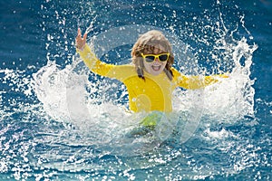 Child splashing in summer water pool. Kid splash in pool. Excited happy kid boy jumping in pool, water fun. Kid jumping