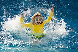 Child splashing in summer water pool. Kid splash in pool. Excited happy little boy jumping in pool, water fun. Kid