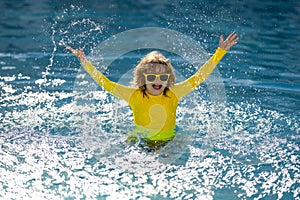 Child splashing in summer water pool. Kid splash in pool. Excited happy little boy jumping in pool, water fun. Kid