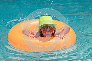 Child splashing and swimming on inflatable toy ring in pool. Vacations and summer recreation with children. Swim water