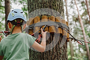 Child in sports equipment, a protective helmet stopped near a tree, holding a rope with his hands. Portrait of a brave boy