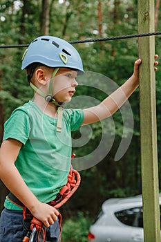 Child in sports equipment, a protective helmet stopped near a tree, holding a rope with his hands. Portrait of a brave boy