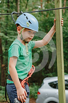 Child in sports equipment, a protective helmet stopped near a tree, holding a rope with his hands. Portrait of a brave boy