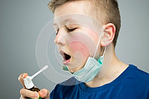 A child sprays a throat with a spray. A child in an antiviral mask