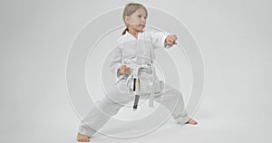 The child spreads his legs wide and strikes with straight hands in front of her. Karate exercises.