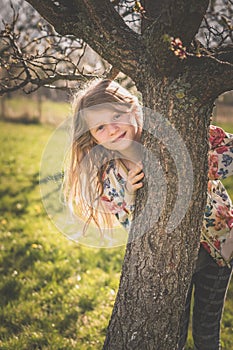 child in spring nature behind the tree trunk