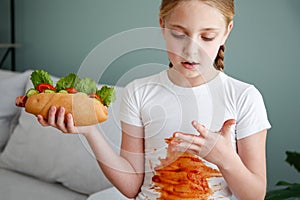 The child stained his clothes with ketchup. A girl eats a hot dog