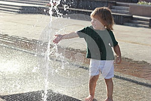 Little cute male baby standing near fountain. Concept of walking in city with children