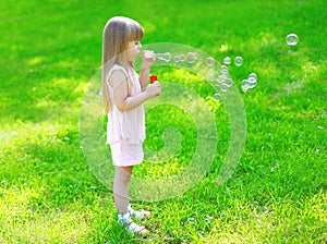 Child standing on the grass blowing soap bubbles in summer