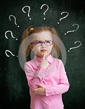 Child standing near school chalkboard with many question marks