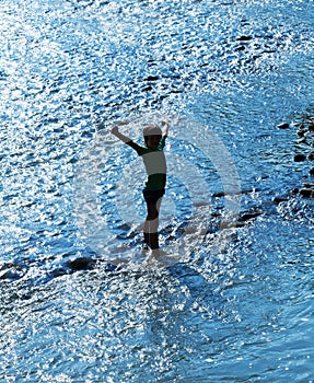 Child standing in water sparkling in backlight