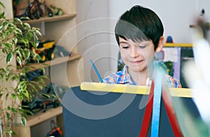 Child standingnext to the easel. Kid boy learn paint by brush in class school. Kindergarten interior on background. Boy