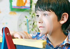 Child standingnext to the easel. Kid boy learn paint by brush in class school. Kindergarten interior on background. Boy