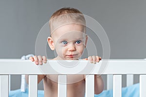 A child stands in a crib and looks with sarcasm like an adult photo