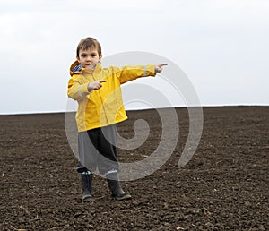 A child stands in a field, pointing his hands to the left