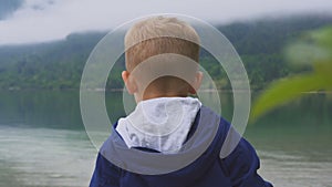 Child stands on rock and looks down at a blue mountain lake. back view.