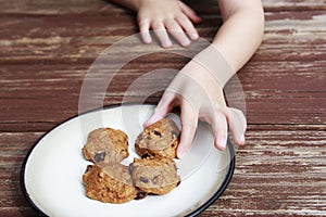 Child stealing a pumpkin chocolate chip cookie from a plate.