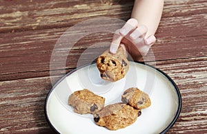 Child stealing a pumpkin chocolate chip cookie from a plate.