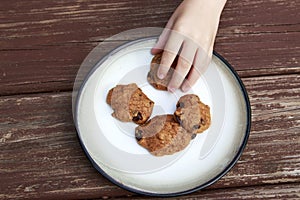 Child stealing a pumpkin chocolate chip cookie from a plate.