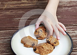 Child stealing a pumpkin chocolate chip cookie from a plate.