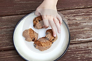 Child stealing a pumpkin chocolate chip cookie from a plate.