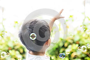 The child stretches out a hand towards the sky. A boy wants to catch soap bubbles