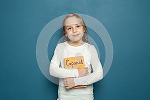 Child student girl with Spanish language book on the background of blue chalkboard