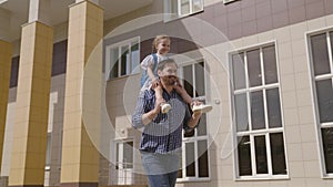 child student with school backpack rides on his father shoulders, dad cheerfully runs with his daughter kid to school