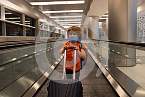 A child with a suitcase at the airport. Protective mask against Covid 19 coronaviruse. Pandemic protection. Empty