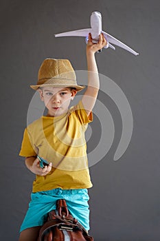 A child in summer clothes and sunglasses sits on a suitcase and holds a toy airplane in his hands. Waiting for travel