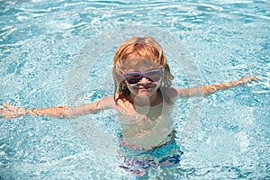 Child in summer swimming pool. Cute boy in the water playing with water. Smiling cute little boy in sunglasses in pool