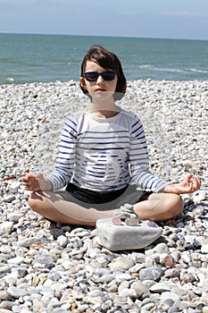 Child with sunglasses meditating with quartz crystals on pebble beach