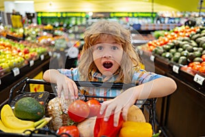 Child in the supermarket. Funny excited little boy wit shopping cart choosing goods at grocery store or supermarket