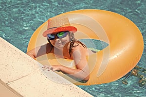 Child in swimming pool on inflatable ring. Kid swim with orange float. Kids beach fun.